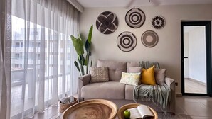 A modern living room with a sofa, two wooden side tables, and a large window with sheer curtains. - 4 Bedroom Beach Penthouse w Private Rooftop (Punta Cana)