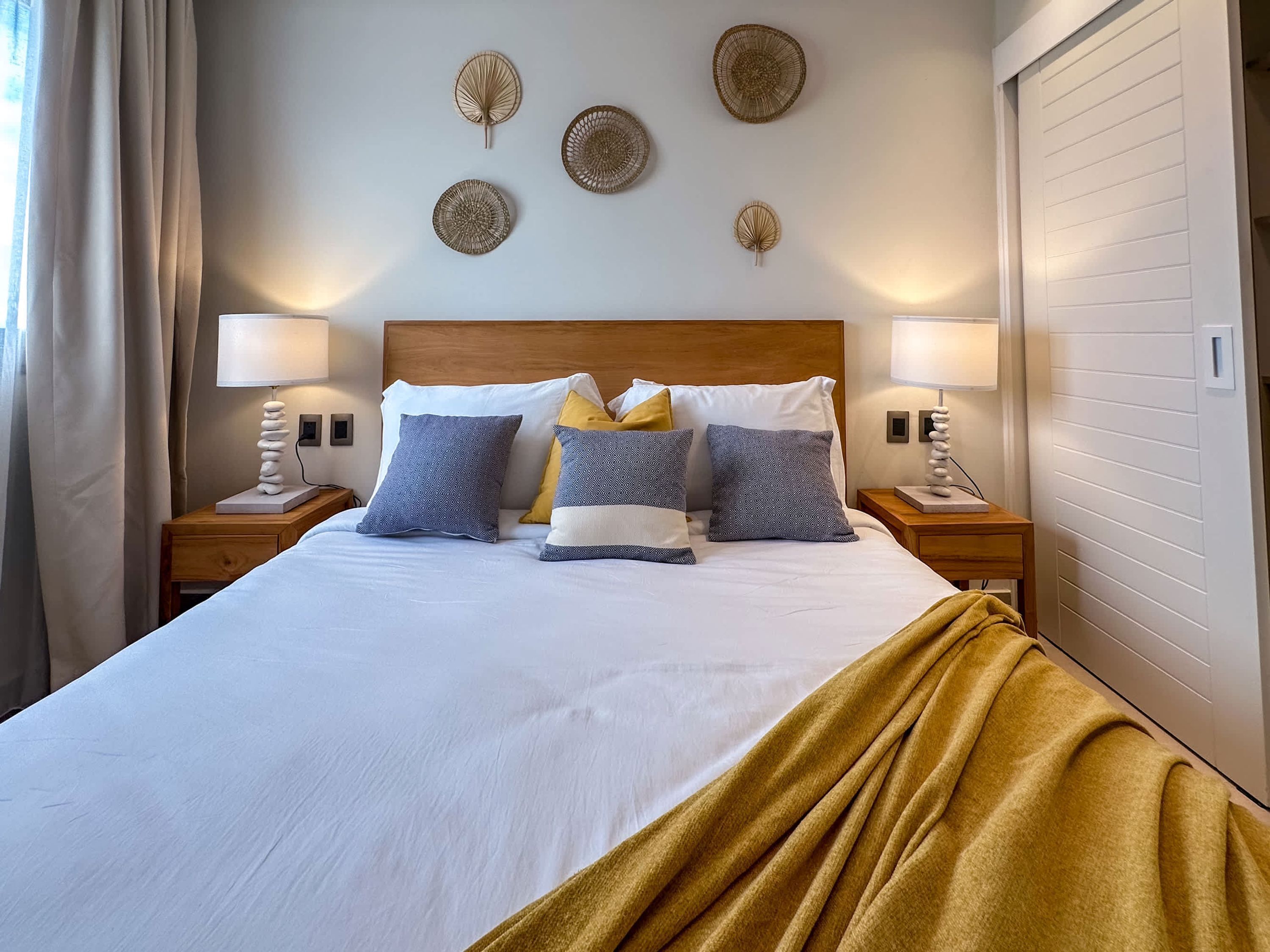 Un letto rifatto con cura, coperto da un piumone bianco, una coperta dorata e cuscini fantasia. Due comodini con lampade e decorazioni a parete sopra il letto.