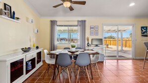 A dining area with a table set for four, a ceiling fan, and a view through a glass door to an outdoor patio. - Desert Oasis Cozy Comfort Meets Outdoor Luxury (Twentynine Palms)