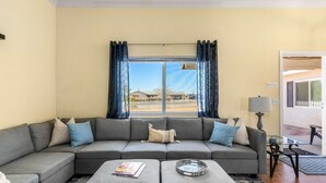 A living room with a grey sectional sofa, a coffee table, and a window with curtains. - Desert Oasis Cozy Comfort Meets Outdoor Luxury (Twentynine Palms)