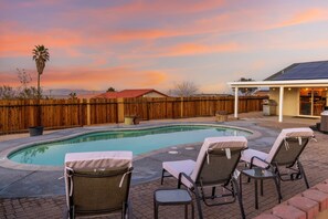 A backyard with a swimming pool, lounge chairs, and a barbecue area. - Desert Oasis Cozy Comfort Meets Outdoor Luxury (Twentynine Palms)