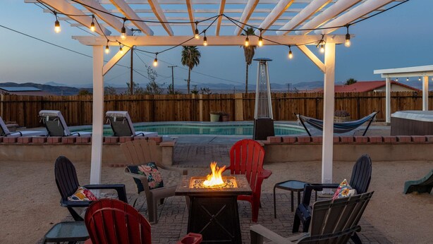 A backyard with a fire pit, outdoor seating, a pool, and a pergola with string lights. - Desert Oasis Cozy Comfort Meets Outdoor Luxury (Twentynine Palms)
