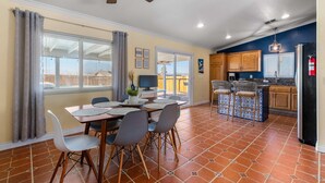 A dining area with a table and chairs, a ceiling fan, and a kitchen with wooden cabinets and a refrigerator. - Desert Oasis Cozy Comfort Meets Outdoor Luxury (Twentynine Palms)