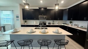 Een moderne keuken met donkere kastjes, een centraal eiland met barkrukken en hanglampen.