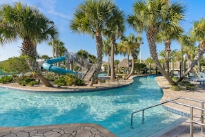 A swimming pool with a blue slide, surrounded by palm trees and lounge chairs.