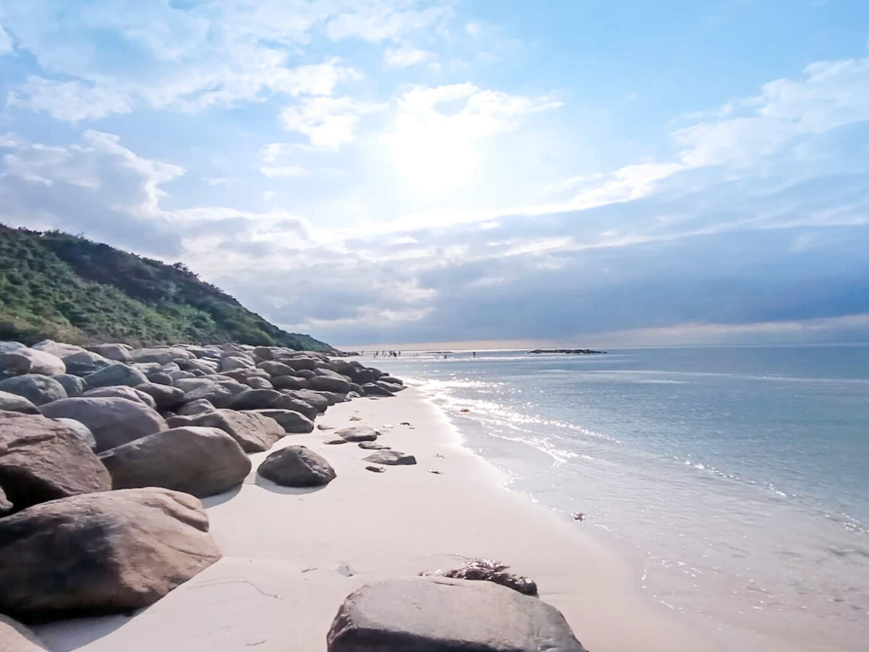A beach with large rocks in the foreground and a clear view of the sea.
