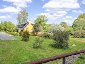 A yellow house with a dark roof, surrounded by a well-maintained lawn and various trees.