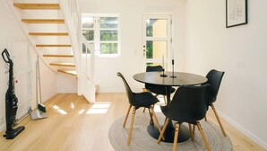A modern dining area with a round table, black chairs, a wooden staircase, and a view of greenery outside. - 5 Star Holiday Home in Liseleje (Liseleje)
