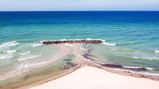 A beach with clear blue water, a rocky breakwater, and a sandy shore. - 5 Star Holiday Home in Liseleje (Liseleje)