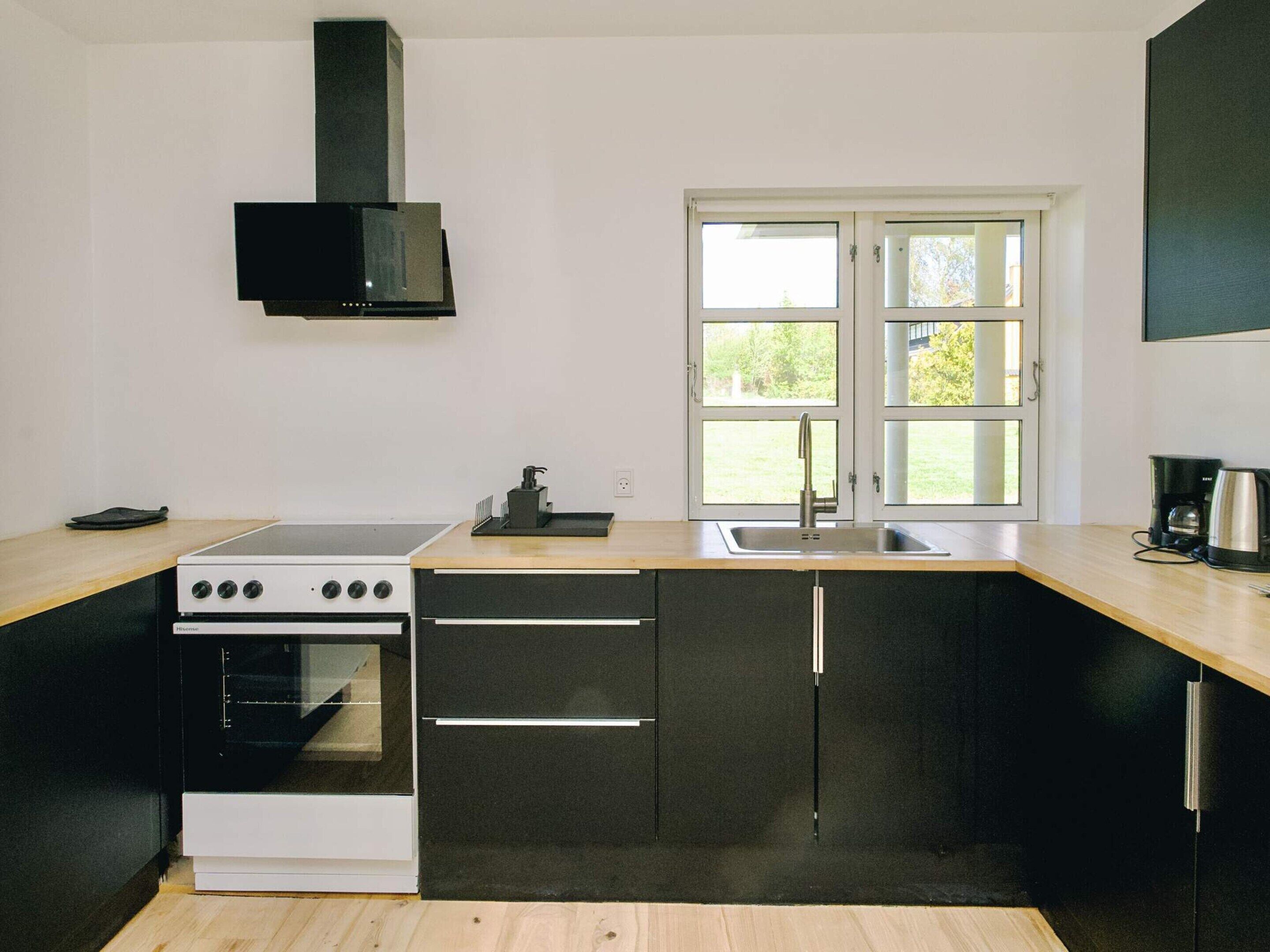 Une cuisine moderne équipée d’une cuisinière, d’un four, d’un évier et d’une fenêtre donnant sur un paysage verdoyant.
