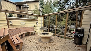Eine Terrasse im Freien mit Steinboden, einer Feuerstelle, Holzbanken und einem Mülleimer.