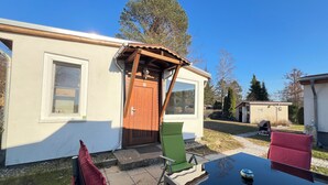 A patio area with a table and chairs, a wooden door, and a small shed in the background. - Cozy bungalow vacation idyll (Koserow)