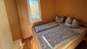 A bedroom with a bed, pillows, a window, and wooden walls. - Cozy bungalow vacation idyll (Koserow)