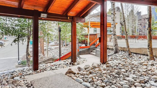 Un espace extérieur abrité, doté de poutres en bois, d’un chemin en pierre et offrant une vue sur une rue bordée de voitures garées et d’arbres.