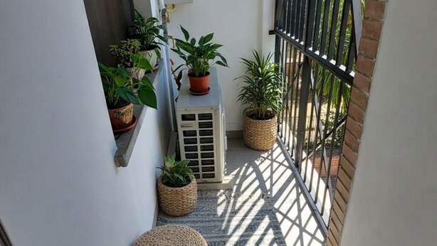 Un balcón estrecho con plantas en macetas, un equipo de aire acondicionado pequeño y un farol.