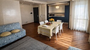 Una sala de estar moderna con una mesa de comedor preparada para cuatro personas, un sofá y una cocina al fondo.