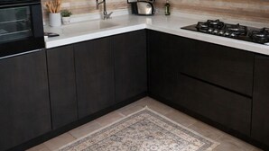 Una cocina moderna con armarios oscuros, encimera blanca, estufa a gas y lámpara colgante.