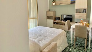 Une chambre d’hôtel comprenant un lit, un bureau avec un ordinateur, une télévision et une petite étagère avec des objets décoratifs.