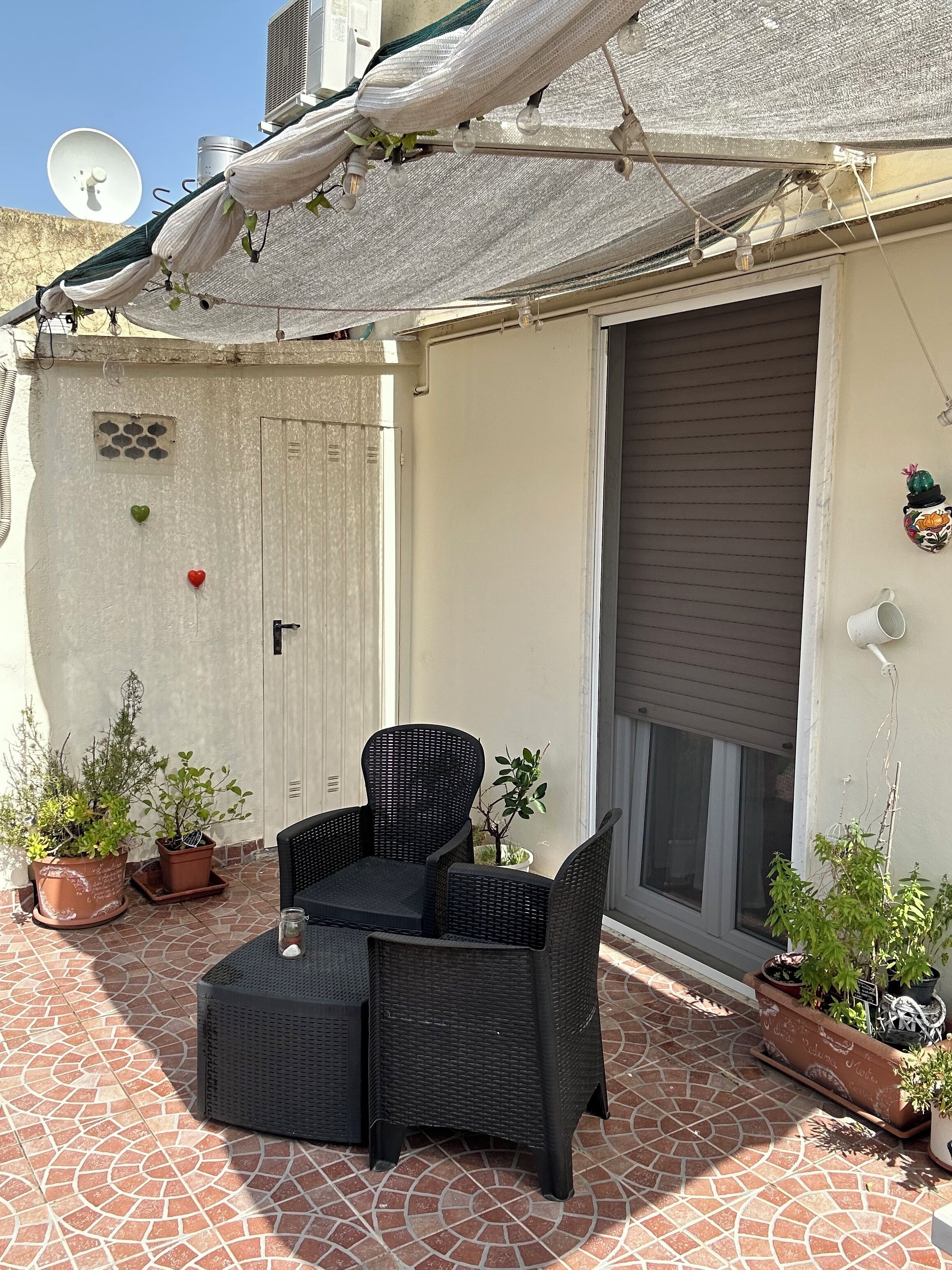 A patio with a black wicker table and chairs, potted plants, and a white door with a window.