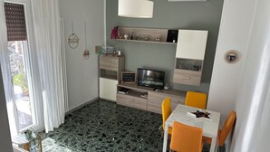 Un salon moderne comprenant un coin repas, un téléviseur et une petite étagère ornée d’objets décoratifs.