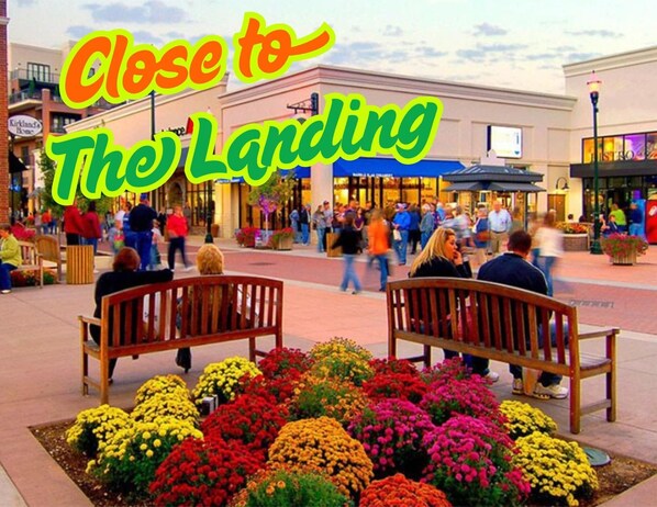 A public square with benches and flower beds, surrounded by shops and a sign indicating proximity to the airport. - 205 Close to downtown, Landing and Convention Center (Branson)