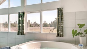 A modern bathroom with a large bathtub, a view of the outdoors through large windows, and a potted plant. - 5 Star Holiday Home in Albaek (Aalbaek)