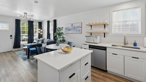 Une cuisine moderne avec des meubles blancs, un four à micro-ondes et un évier. On y trouve également un coin repas avec une table ronde et des chaises bleues.