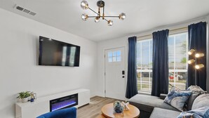 Un salon moderne doté d’un téléviseur à écran plat, d’une cheminée, d’un canapé bleu et d’un luminaire suspendu au plafond.
