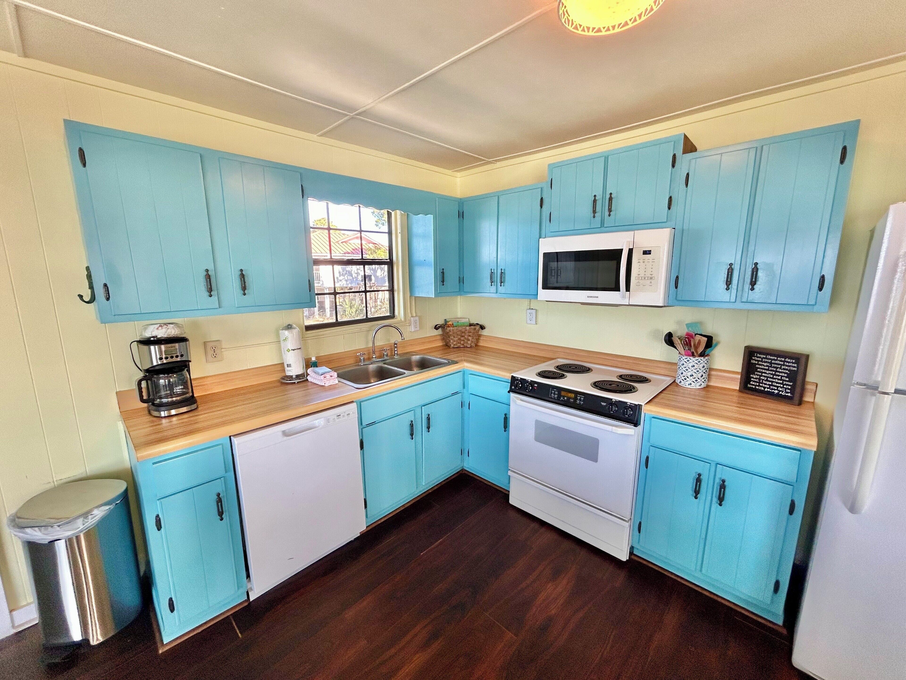 A kitchen with teal cabinets, a microwave, a stove, and a coffee maker.