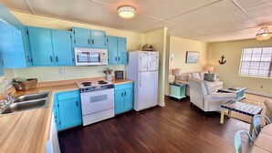 A compact kitchen with blue cabinets, a microwave, a stove, and a refrigerator. - Bayside Cottage bayfront home with private dock (St. George Island)
