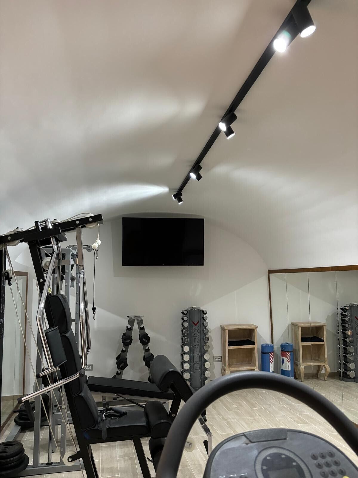 Een sportschool met trainingsapparatuur, een aan de muur bevestigde televisie en een spiegel.