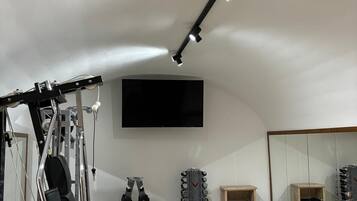 Een sportschool met trainingsapparatuur, een aan de muur bevestigde televisie en een spiegel.
