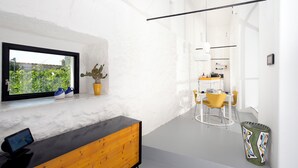 A modern interior with a wooden bench, a dining area with yellow chairs, a kitchen in the background, and a window with a view of greenery. - Capri Kronos Design Suites (Anacapri)