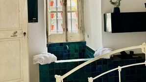 A bedroom with a bed, a window with potted plants, a white door, and a black shelf. - Capri Kronos Design Suites (Anacapri)