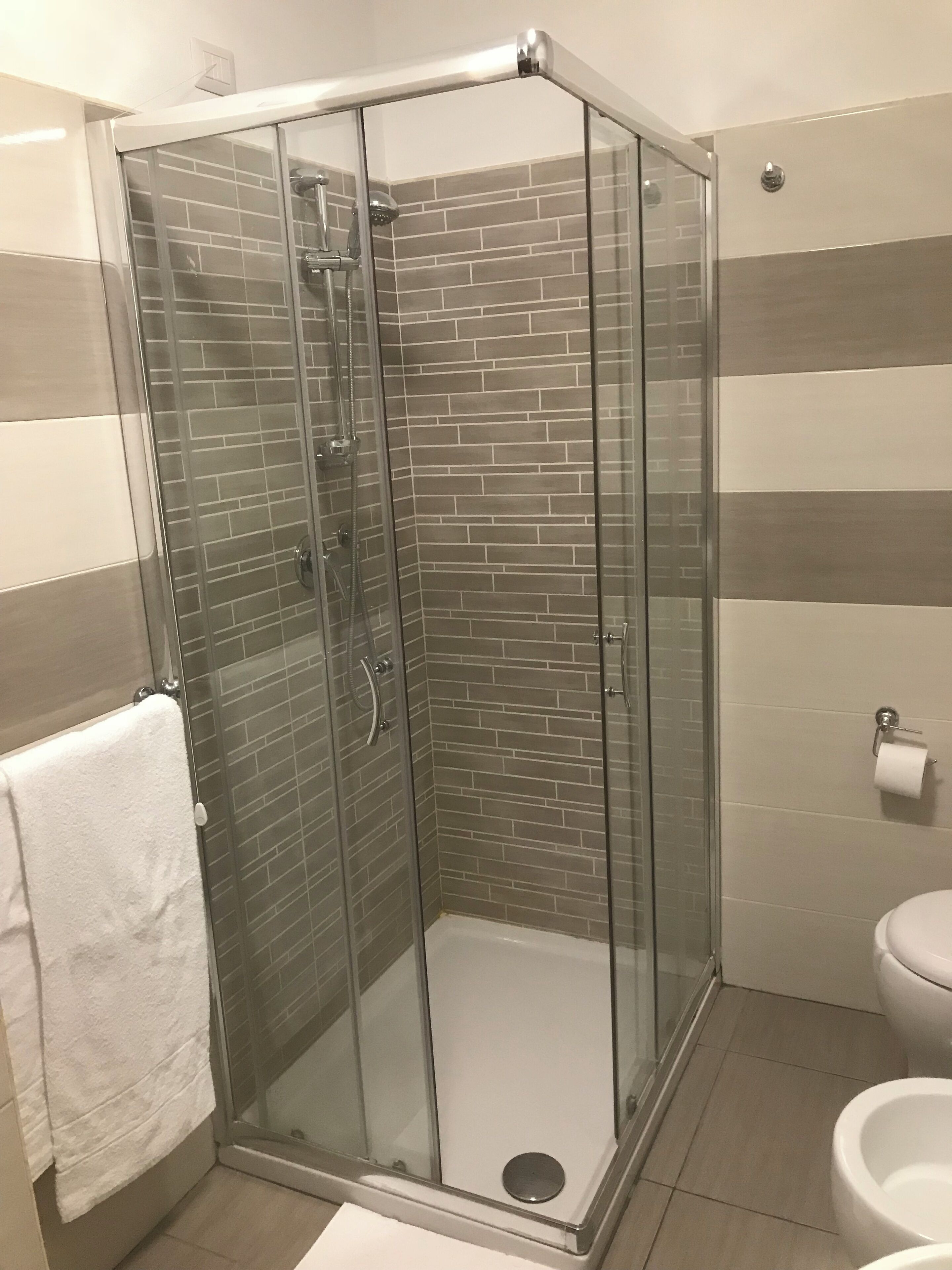 A glass-enclosed shower stall with a tiled wall, a white toilet, and a towel hanging on the wall.