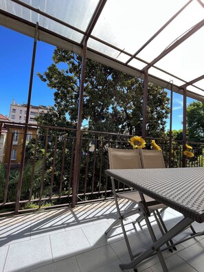 A covered outdoor seating area with a table and chairs, surrounded by a metal railing and a glass canopy. - Appartamenti Aspromonte (Milan)