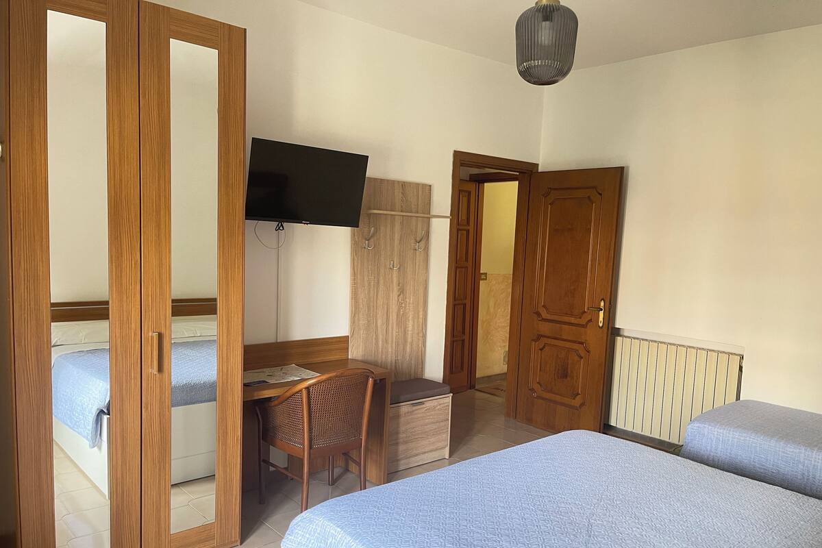 A bedroom with a bed, a desk with a chair, a television, and a wardrobe.