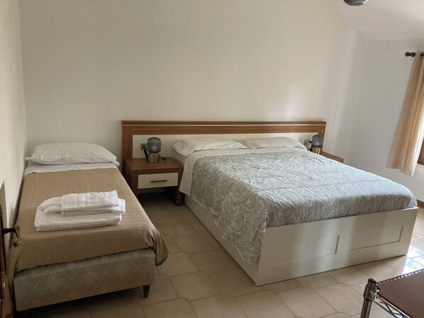 Habitación de hotel con dos camas, una mesita de noche con lámpara y una silla.