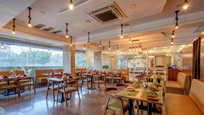 A spacious restaurant with multiple dining areas, large windows, and hanging light fixtures. - W Hotel Shamshabad Hyderabad Airport (Hyderabad)