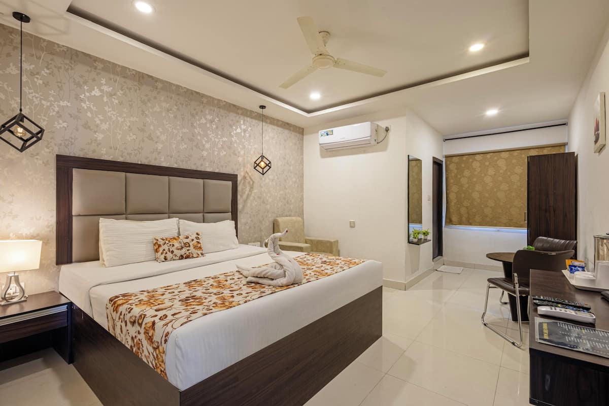 A modern hotel room with a large bed, a desk with a chair, a ceiling fan, and an air conditioning unit.