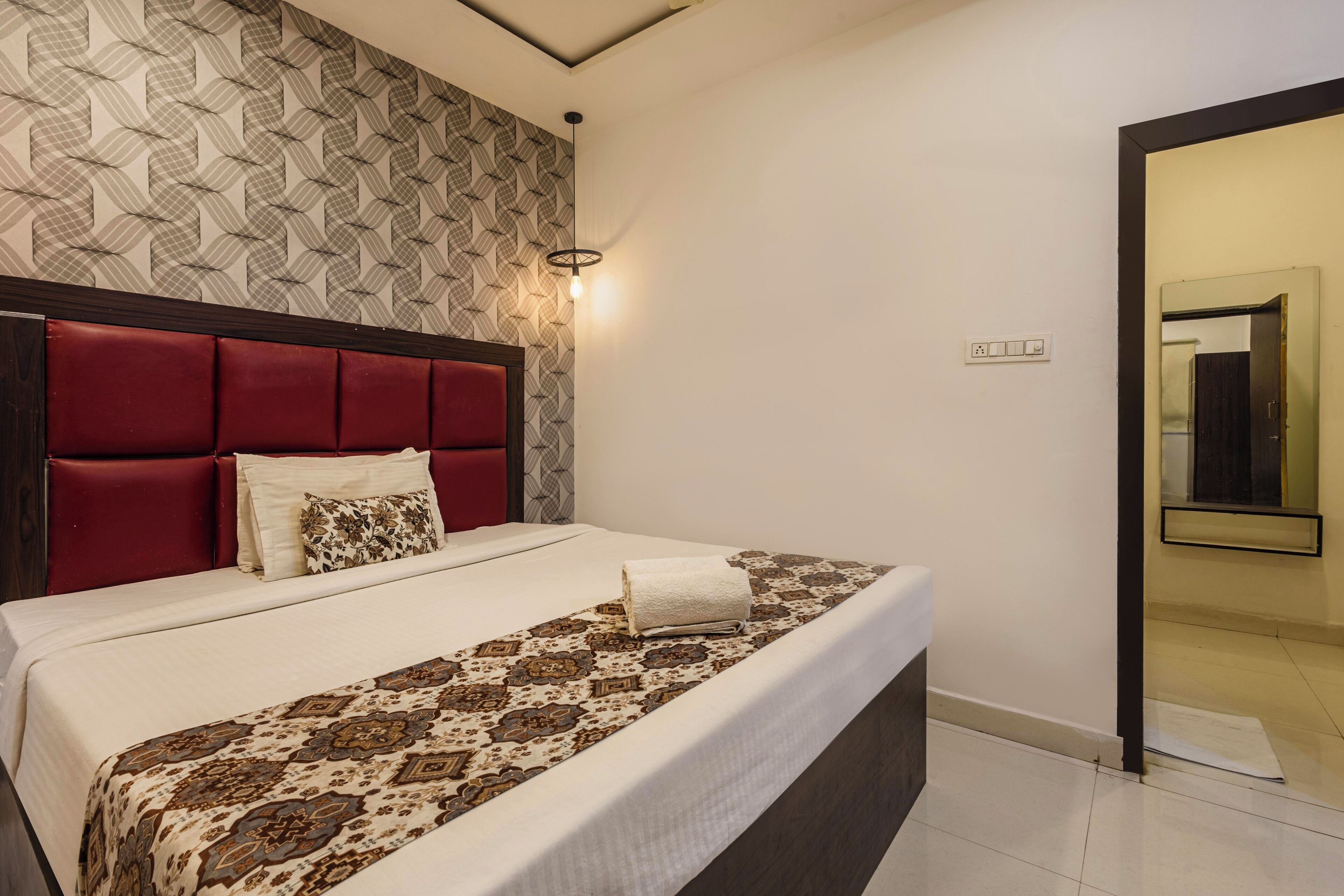 Un letto ben rifatto con copriletto decorato, una testiera rossa e un muro rivestito con carta da parati a motivi geometrici.