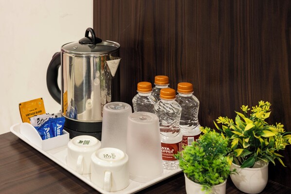 Una bandeja con tetera, botellas de agua, cafetera y una pequeña planta.