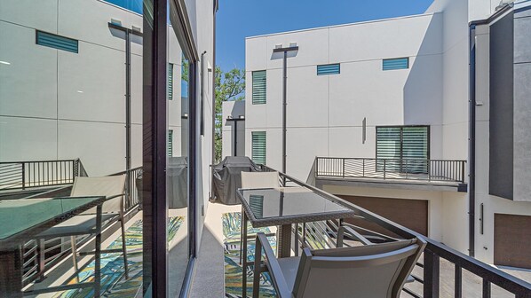 A modern outdoor seating area with a table and chairs, a covered grill, and a view of adjacent buildings.