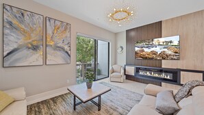 A modern living room with a fireplace, a TV mounted on the wall, and abstract art on the wall. - Uptown Oasis 3 Bedroom Townhouse (Sarasota)