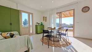 A modern room with a bed, a dining table with chairs, a green cabinet, and large windows. - Tenuta alle Macchie, swimming pool, 4 guests, two bedrooms (Racale)