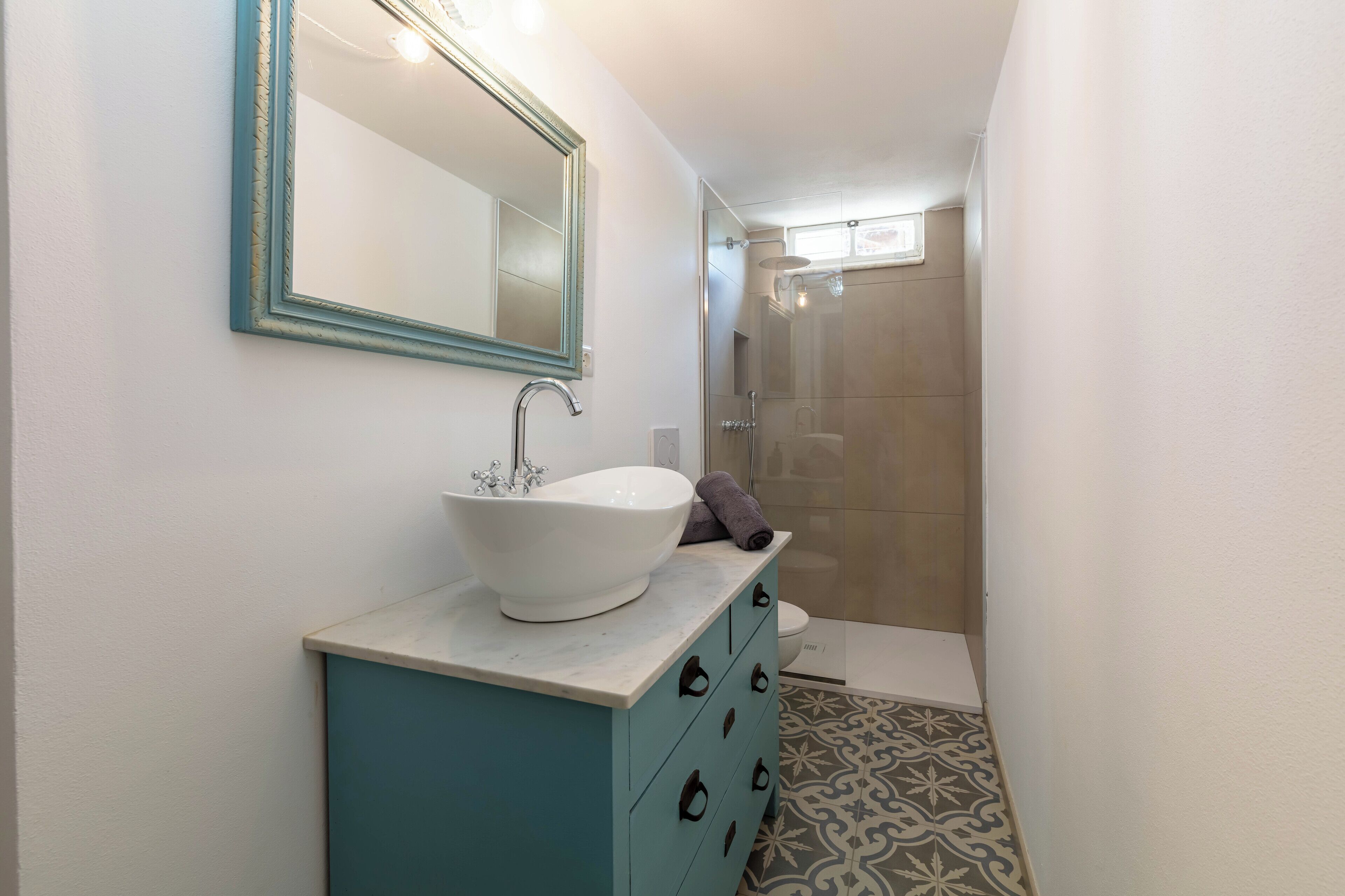 Ein Badezimmer mit einem weißen Waschbecken, einem türkisblauen Schrank und einem Spiegel mit blauem Rahmen.