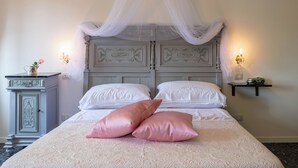 Un dormitorio con cama con dosel, ropa de cama blanca y un cabecero decorativo.