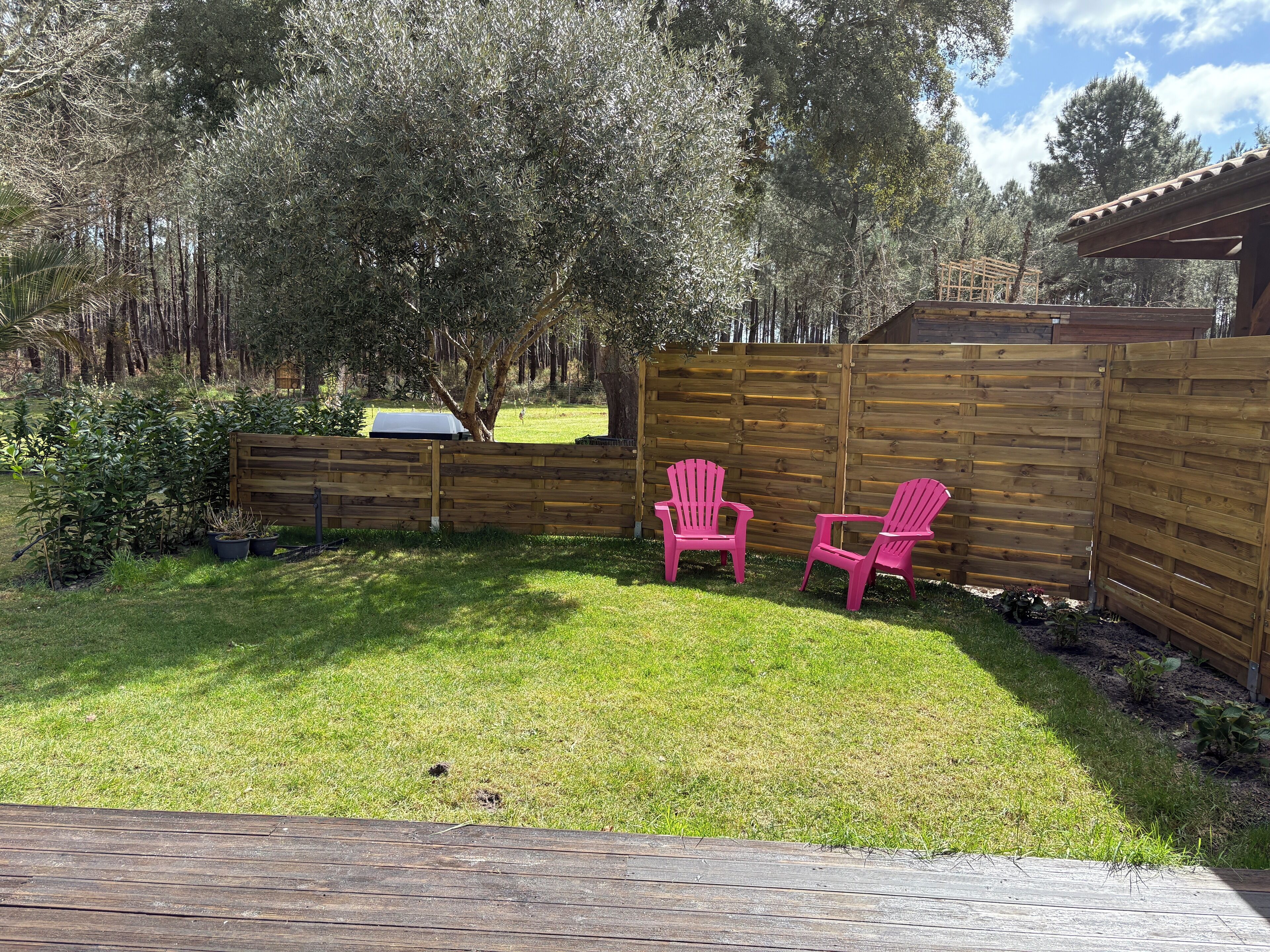 A backyard with a wooden fence, two pink Adirondack chairs, and a small garden area.