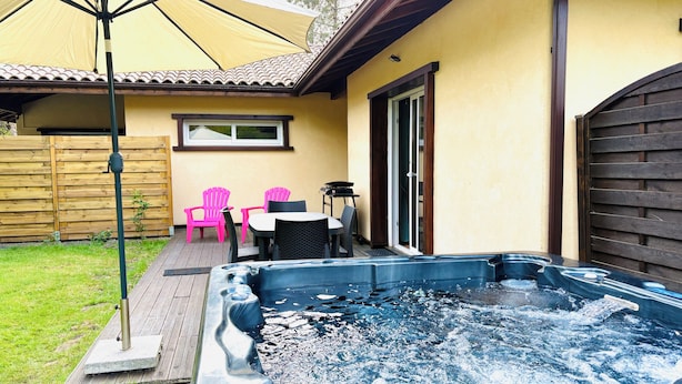 Ein Whirlpool in einem Garten mit einer Holzterrasse, einem Sonnenschirm und einem Tisch mit Stühlen.