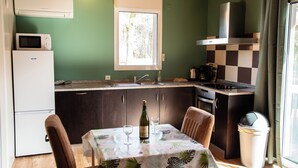 Eine kompakte Küche mit Fenster, einer Mikrowelle, einem Kühlschrank und einem Tisch mit zwei Weingläsern und einer Weinflasche.